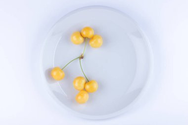 Beyaz tabak, beyaz zemin üzerine taze kiraz, Minimalizm tarzı, vejetaryen yemek, izole sarı çilek Sarı kiraz