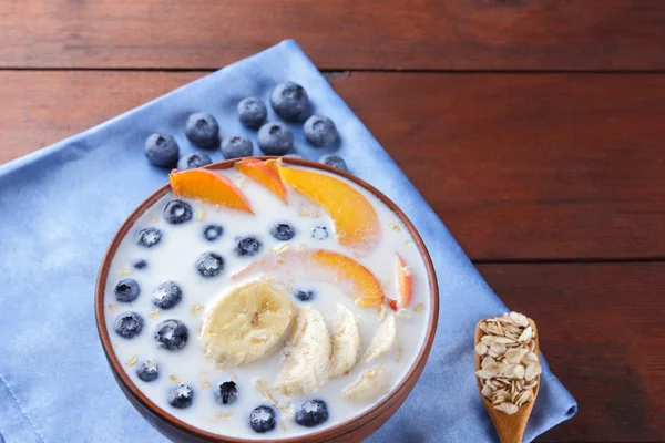 Oatmeal porridge with milk and fruits on a blue napkin, blueberry on wooden boards, vegetarian food on textiles, useful porridge with pieces of banana and peach