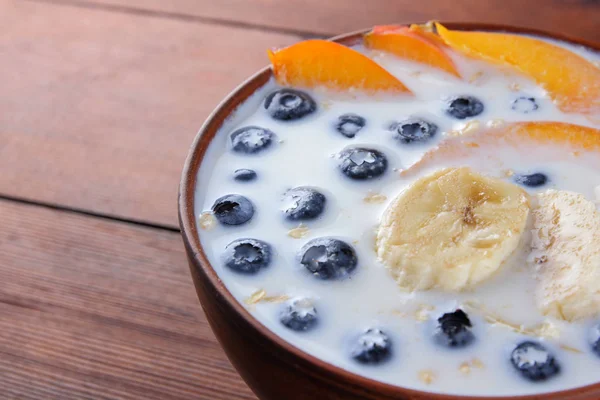 Oatmeal porridge with milk and fruit on a wooden background, healthy porridge with pieces of banana and peach, breakfast with fiber, calcium and vitamins, food for the schoolboy