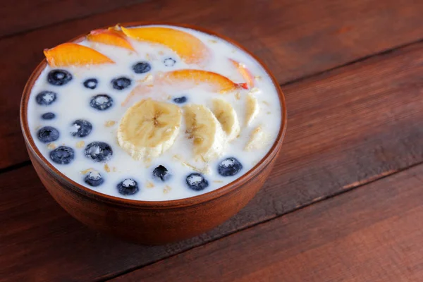 Oatmeal porridge with milk and fruit on wooden background, healthy porridge with pieces of banana and peach, breakfast with fiber, calcium and vitamins