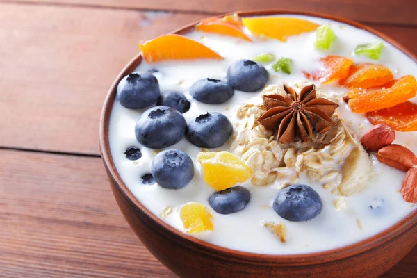 Oatmeal porridge with milk, fruits and peanuts on wooden background, healthy porridge with banana and peach slices, anise, dried apricots in milk