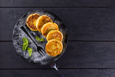 Süzme peynir karanlık bir arka plan üzerinde krep. Geleneksel Ukrayna çanak - taze nane ile syrniki. Siyah bir plaka üzerinde süzme peynir ile Pancakes ile pudra şekeri serpilir. Kopya alanı