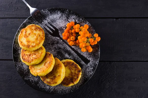 Cottage cheese pancakes on a dark background. Traditional Ukrainian dish - syrniki with fresh mint. Pancakes with cottage cheese on a black plate sprinkled with powdered sugar. Copy space