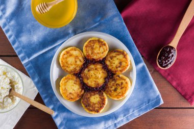 Süzme peynir mavi ve kırmızı peçeteler krep. Geleneksel Ukrayna çanak - reçel ahşap zemin ile syrniki. Süzme peynir beyaz tabakta bal ve rowan ile krep. Kopya alanı