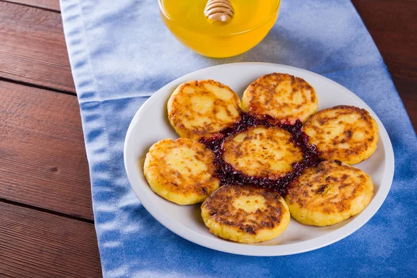 Cottage cheese pancakes on blue napkin. Traditional Ukrainian dish - syrniki with jam on a wooden background. Pancakes with cottage cheese on a white plate with honey. Copy space
