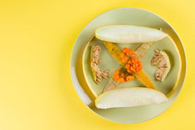 Dilimler ve sarı bir arka plan üzerinde bir kavun içi. Yeşil bir tabakta kavun cilt. Üvez meyveleri renkli bir arka plan üzerinde. Vejetaryen yiyecekler. Yaşam sağlıklı şekilde. Pop Art