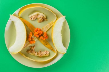 Dilimler ve yeşil bir arka plan üzerinde bir kavun içi. Yeşil bir tabakta kavun cilt. Üvez meyveleri renkli bir arka plan üzerinde. Vejetaryen yiyecekler. Yaşam sağlıklı şekilde. Pop Art