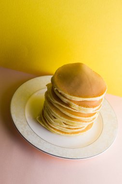 Krep pembe sarı bir arka plan üzerinde. Birçok krep kopya alanı ile beyaz tabakta. Pop sanat tarzı kahvaltı için lezzetli yemek. Renkli arka plan üzerinde şenlikli gıda