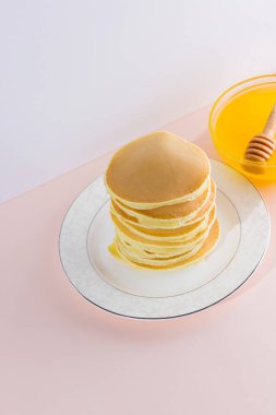 Krep pembe beyaz bir arka plan üzerinde. Kopya alanı ile beyaz tabakta bal ile sıcak krep. Pop sanat tarzı kahvaltı için lezzetli yemek. Tatlım bir tabak üzerinde tahta bir sopa aşağı akar