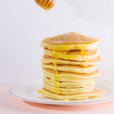 Krep pembe beyaz bir arka plan üzerinde. Kopya alanı ile beyaz tabakta bal ile sıcak krep. Pop sanat tarzı kahvaltı için lezzetli yemek. Tatlım bir tabak üzerinde tahta bir sopa aşağı akar