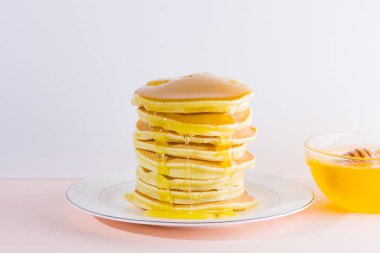 Krep pembe beyaz bir arka plan üzerinde. Kopya alanı ile beyaz tabakta bal ile sıcak krep. Pop sanat tarzı kahvaltı için lezzetli yemek. Tatlım bir tabak üzerinde tahta bir sopa aşağı akar