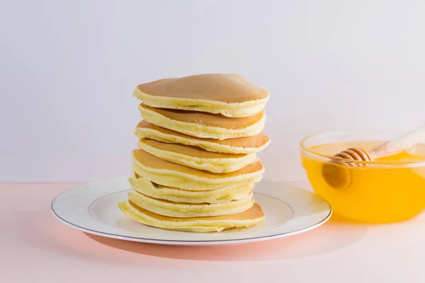 白ピンクの背景のパンケーキ コピー スペースを白い板の上に蜂蜜とホットケーキ ポップアートのスタイルで朝食をおいしい料理 皿の上の木の棒から流れて蜂蜜 — ストック写真