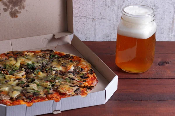 Beer and pizza. Italian pizza in a cardboard box. Light unfiltered beer on a wooden background. Favorite food set for men. Copy space