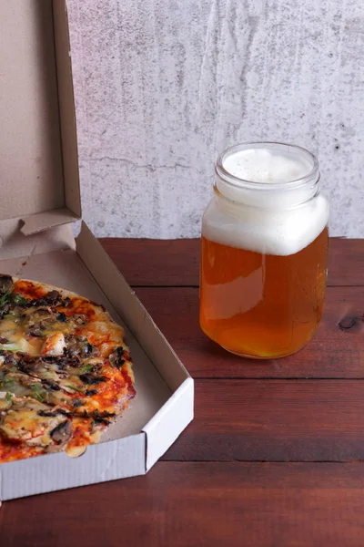 Beer and pizza. Italian pizza in a cardboard box. Light unfiltered beer on a wooden background. Favorite food set for men. Copy space