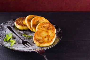 Süzme peynir karanlık bir arka plan üzerinde krep. Geleneksel Ukrayna çanak - taze nane ile syrniki. Siyah bir plaka üzerinde süzme peynir ile Pancakes ile pudra şekeri serpilir