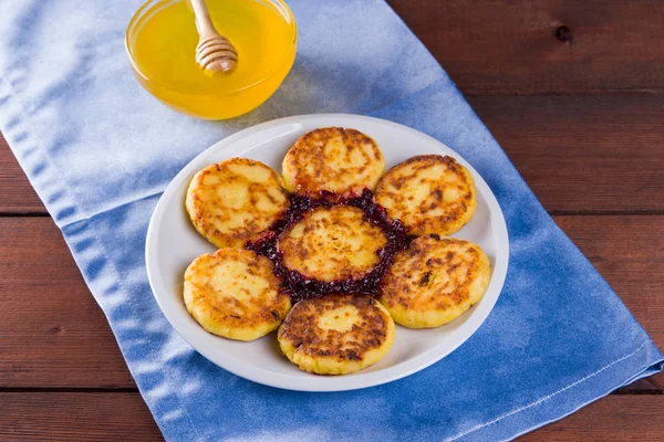Cottage cheese pancakes on blue napkin. Traditional Ukrainian dish - syrniki with jam on a wooden background. Pancakes with cottage cheese on a white plate with honey