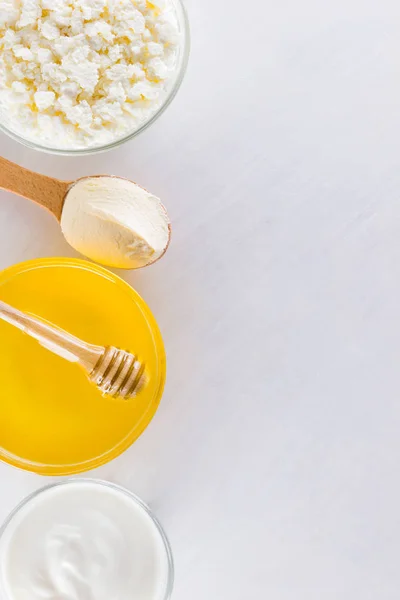 Milk products and honey with wooden cutlery. Cottage cheese, sour cream, cream on a white background top view. Different natural products for vegan. Healthy food