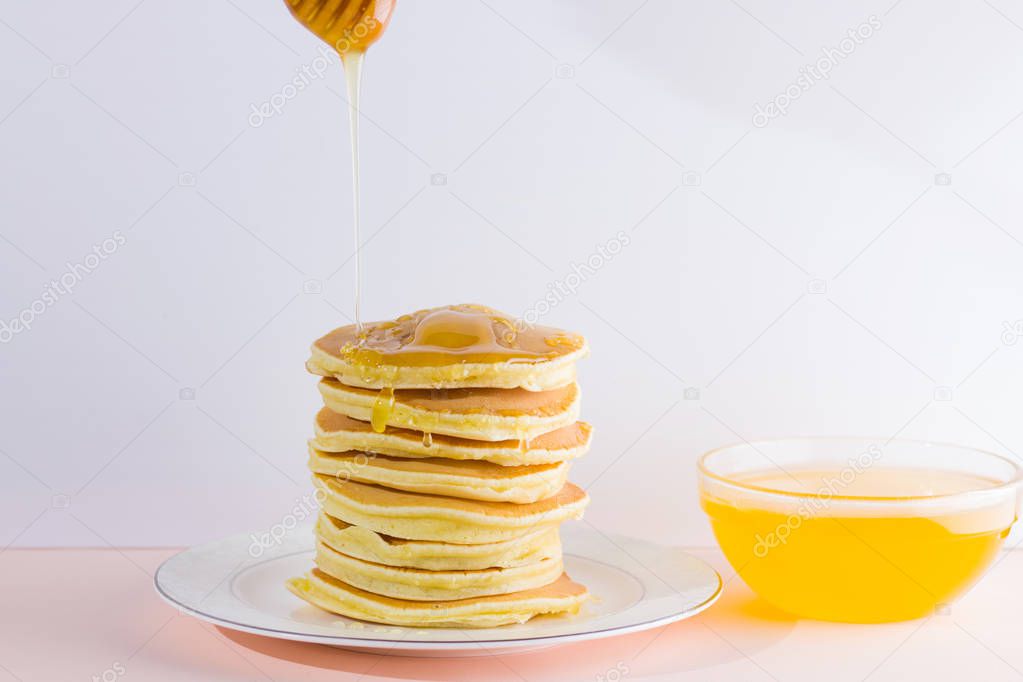Pancakes on a white pink background. Hot pancakes with honey on a white plate with copy space. Delicious dish for breakfast. Honey flows down from a wooden stick on a dish