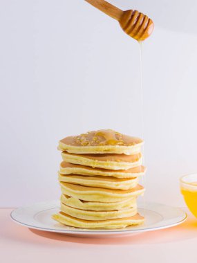 Krep pembe beyaz bir arka plan üzerinde. Kopya alanı ile beyaz tabakta bal ile sıcak krep. Kahvaltı için lezzetli yemek. Tatlım bir tabak üzerinde tahta bir sopa aşağı akar