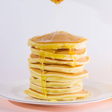Krep pembe beyaz bir arka plan üzerinde. Kopya alanı ile beyaz tabakta bal ile sıcak krep. Kahvaltı için lezzetli yemek. Tatlım bir tabak üzerinde tahta bir sopa aşağı akar