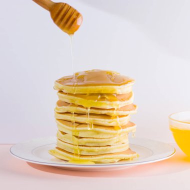 Krep pembe beyaz bir arka plan üzerinde. Kopya alanı ile beyaz tabakta bal ile sıcak krep. Kahvaltı için lezzetli yemek. Tatlım bir tabak üzerinde tahta bir sopa aşağı akar