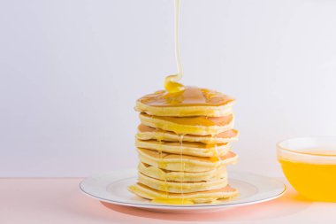 Krep pembe beyaz bir arka plan üzerinde. Kopya alanı ile beyaz tabakta bal ile sıcak krep. Kahvaltı için lezzetli yemek. Tatlım bir tabak üzerinde tahta bir sopa aşağı akar