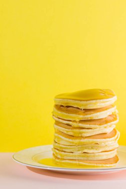 Sarı pembe bir arka plan üzerinde ballı krep. İştah açıcı krep yerken üzerine beyaz plaka ve bal. Pop sanat tarzı kahvaltı için lezzetli yemek