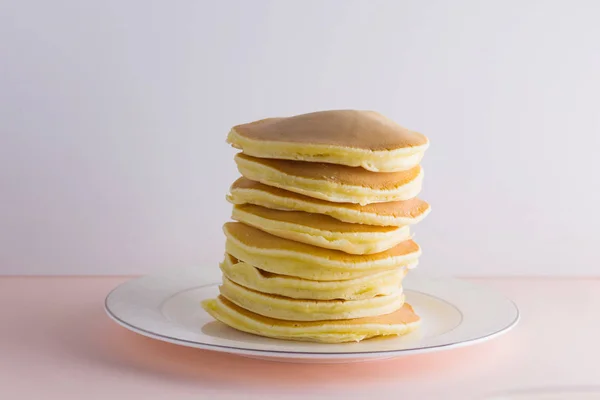 Pancakes on a white pink background. Hot pancakes with honey on a white plate with copy space. Delicious dish for breakfast. Honey flows down from a wooden stick on a dish