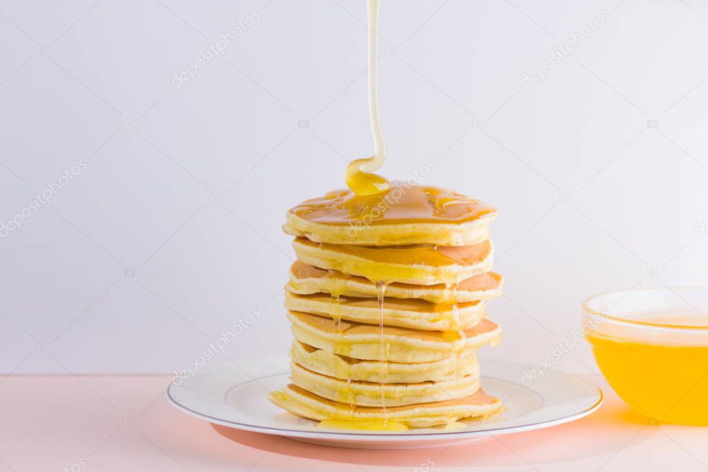 Pancakes on a white pink background. Hot pancakes with honey on a white plate with copy space. Delicious dish for breakfast. Honey flows down from a wooden stick on a dish