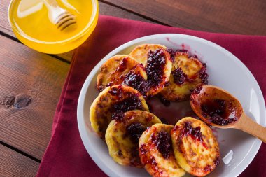 Süzme peynir bir ahşap arka plan üzerinde krep. Syrniki kırmızı peçeteye reçelli. Bal ve rowan ile beyaz bir plaka üzerinde süzme peynir ile çilek krep. Sağlıklı gıda