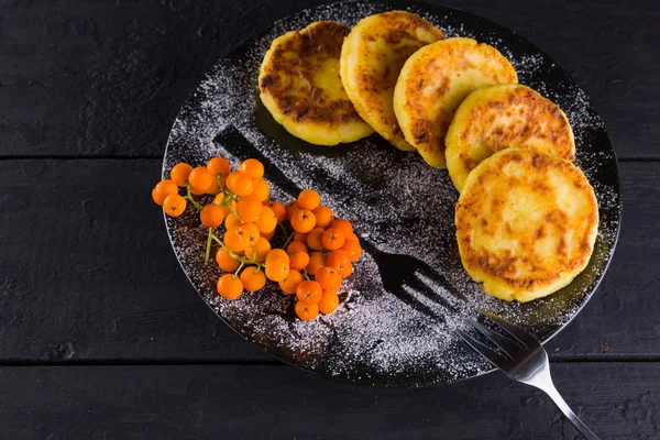 Cottage cheese pancakes on a dark background. Syrniki with fresh mint. Pancakes with cottage cheese on a black plate sprinkled with powdered sugar. Healthy food