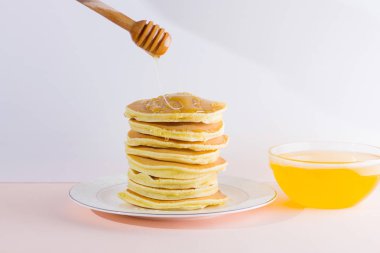 Krep pembe beyaz bir arka plan üzerinde. Beyaz tabakta bal ile sıcak krep. Kahvaltı için lezzetli yemek. Tatlım bir tabak üzerinde tahta bir sopa aşağı akar. Sağlıklı gıda