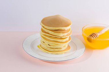 Krep pembe beyaz bir arka plan üzerinde. Beyaz tabakta bal ile sıcak krep. Kahvaltı için lezzetli yemek. Tatlım bir tabak üzerinde tahta bir sopa aşağı akar. Sağlıklı gıda