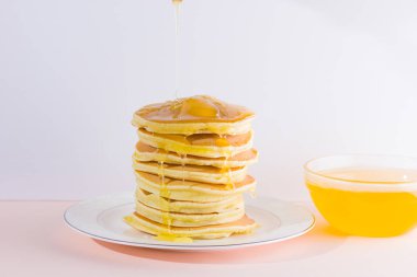 Krep pembe beyaz bir arka plan üzerinde. Beyaz tabakta bal ile sıcak krep. Kahvaltı için lezzetli yemek. Tatlım bir tabak üzerinde tahta bir sopa aşağı akar. Sağlıklı gıda