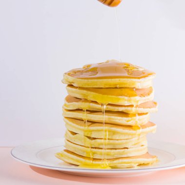 Krep pembe beyaz bir arka plan üzerinde. Beyaz tabakta bal ile sıcak krep. Kahvaltı için lezzetli yemek. Tatlım bir tabak üzerinde tahta bir sopa aşağı akar. Sağlıklı gıda