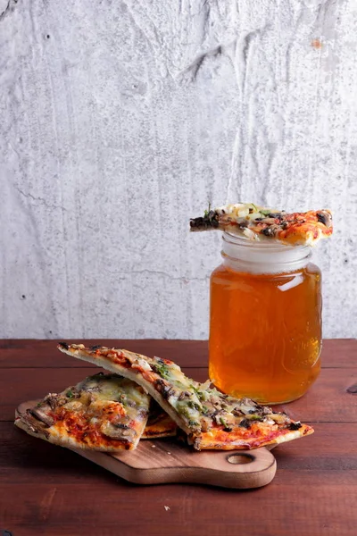 Beer and pizza. Pizza slices on a wooden board. Glass of light beer with foam on a wooden background. Simple food for men