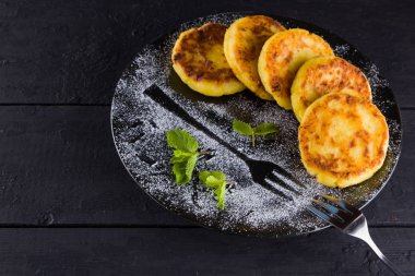 Koyu arkaplanda süzme peynirli krep. Nane şekerli Syrniki. Siyah tabakta süzme peynirli krepler üzerine pudra şekeri serpilmiş. Ev yapımı yemek.