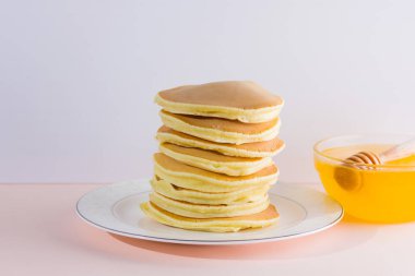 Krep pembe beyaz bir arka plan üzerinde. Beyaz tabakta bal ile sıcak krep. Kahvaltı için lezzetli yemek. Tatlım bir tabak üzerinde tahta bir sopa aşağı akar. Ev yapımı yiyecek
