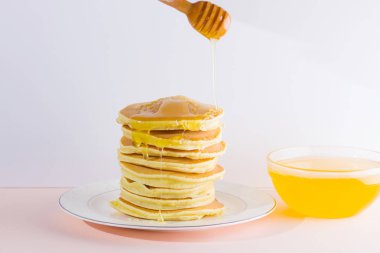Krep pembe beyaz bir arka plan üzerinde. Beyaz tabakta bal ile sıcak krep. Kahvaltı için lezzetli yemek. Tatlım bir tabak üzerinde tahta bir sopa aşağı akar. Ev yapımı yiyecek