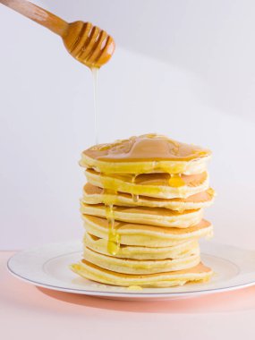 Krep pembe beyaz bir arka plan üzerinde. Beyaz tabakta bal ile sıcak krep. Kahvaltı için lezzetli yemek. Tatlım bir tabak üzerinde tahta bir sopa aşağı akar. Ev yapımı yiyecek