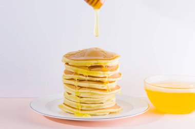 Krep pembe beyaz bir arka plan üzerinde. Beyaz tabakta bal ile sıcak krep. Kahvaltı için lezzetli yemek. Tatlım bir tabak üzerinde tahta bir sopa aşağı akar. Ev yapımı yiyecek