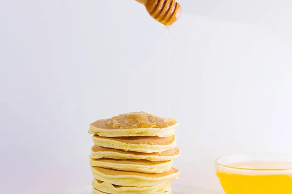 Pancakes on a white pink background. Hot pancakes with honey on a white plate. Delicious dish for breakfast. Honey flows down from a wooden stick on a dish. Homemade food