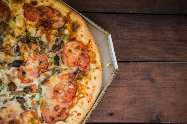 Pizza rustik tarzı ahşap arka plan üzerinde. İtalyan pizza dükkanı işleten bir karton kutu içinde. Ahşap arka plan üzerinde basit gıda