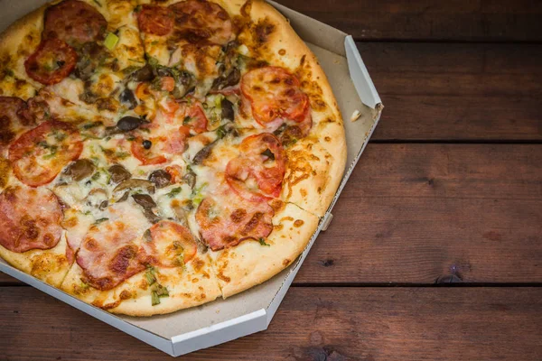 Pizza rustik tarzı ahşap arka plan üzerinde. İtalyan pizza dükkanı işleten bir karton kutu içinde. Ahşap arka plan üzerinde basit gıda