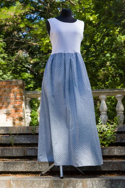Summer long dress of jersey. White blue dress on mannequin. Female sarafan made of natural fabric. Natural background. Copy space