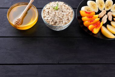 Yulaf ezmesi, bal ve kahvaltı için nane ile dilimlenmiş meyve. Yulaf gevreği, muz dilimleri, dilimlenmiş elma ve şeftali. Yulaf ezmesi, çeşitli meyve ve siyah ahşap kurullarında tatlım. Sağlıklı gıda