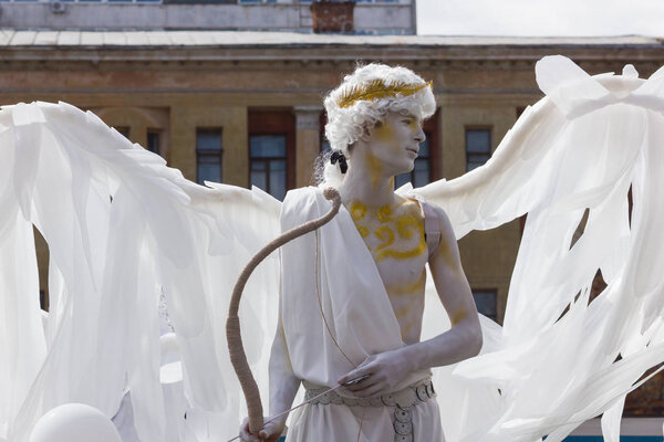 Человек в костюме ангела. Белый ангел с крыльями и луком. Древний греческий бог с луком в руке. Карнавальная процессия "Я люблю Днепр". Украина, Днепр, 8 сентября 2018
