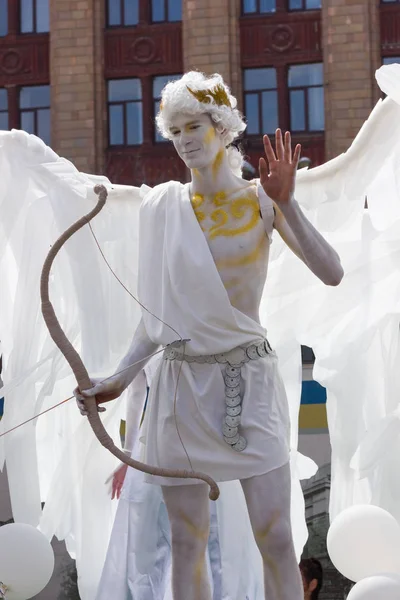 Man in costume of angel. White angel with wings and bow. Ancient Greek god with bow in hand. Carnival procession 
