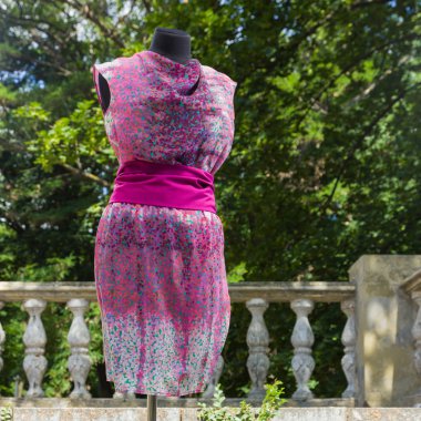 Pembe elbiseyi mankeni. Pembe yeşil yaz sarafan. Kadın el yapımı giysileri ile geniş bant. Çok renkli elbise doğal zemin üzerine Satılık