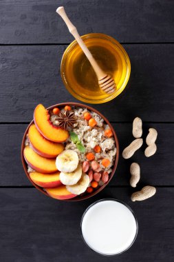 Yulaf ezmesi ve süt, meyve ve koyu ahşap kurullarında tatlım. Yulaf ezmesi, fıstık ve meyve bal ile kahvaltıda pişmiş. Şeftali, muz, nane ve yulaf lapası ile dağ kül